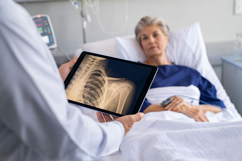 A doctor examines a woman’s x-ray beside her hospital bed.