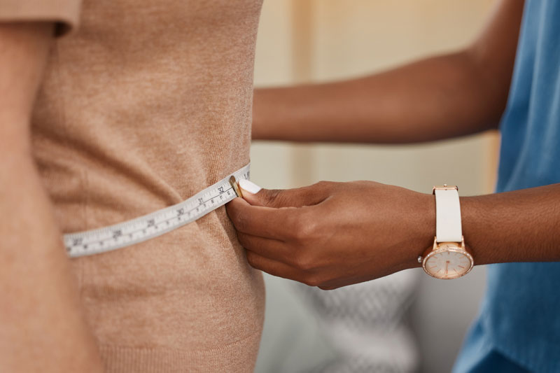A doctor evaluates a patient's weight loss by encircling their midsection with a measuring tape.