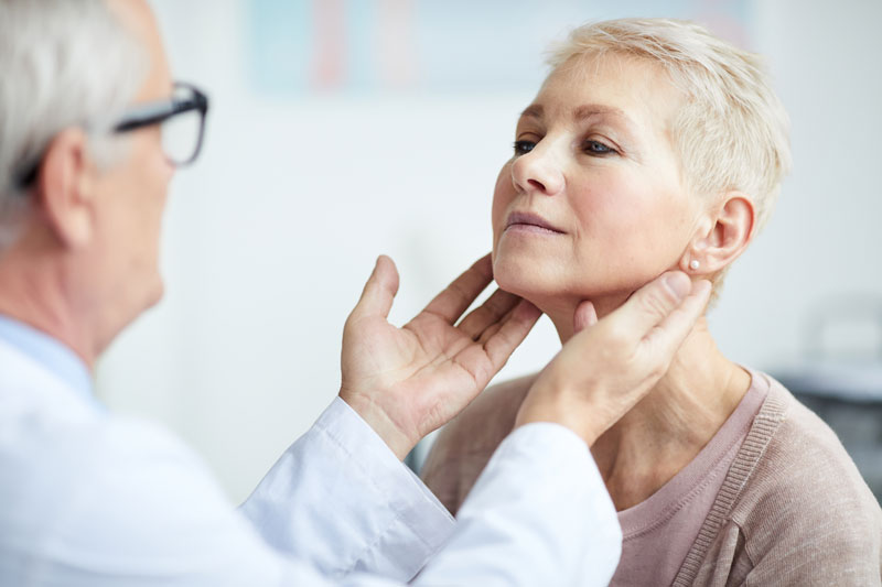 A doctor examines a woman's thyroid and neck area during a medical visit.