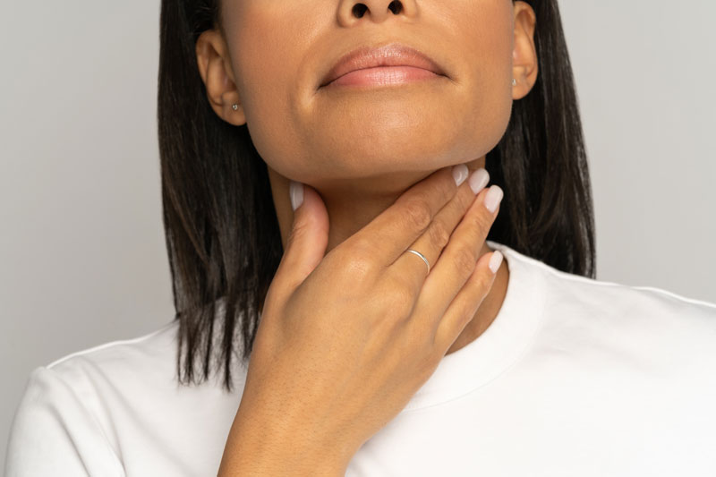 A woman touches her hand to her thyroid and throat area.