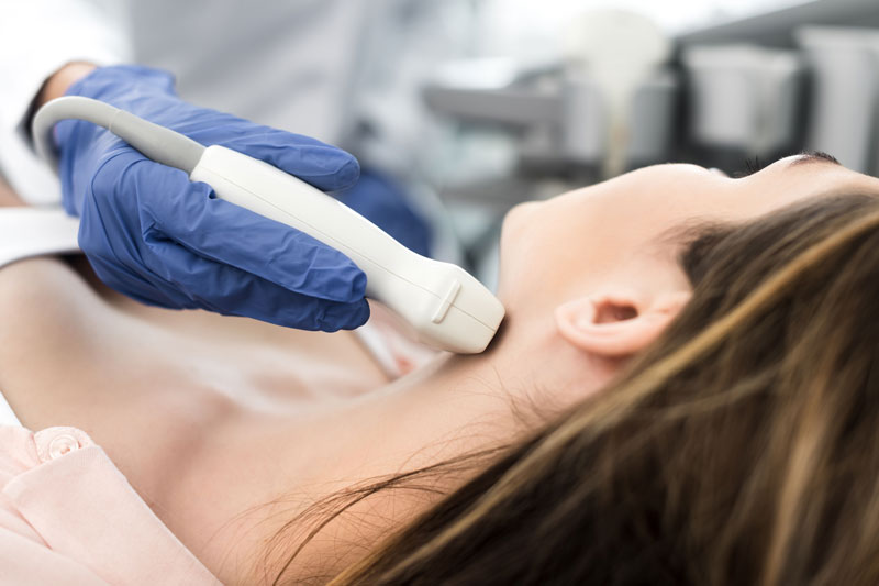 A nurse examines a senior man's thyroid and neck with her hands during a medical exam.