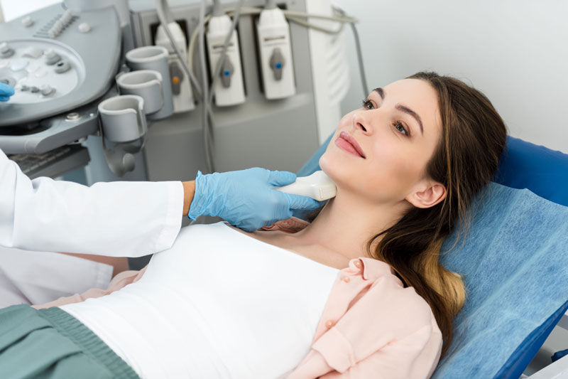 A patient smiles as a doctor performs an ultrasound scan on her thyroid.