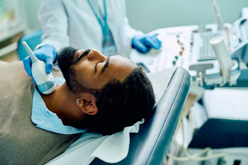 A man receives a thyroid ultrasound in a medical office setting.