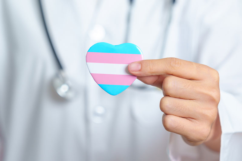 A doctor holds up a small heart striped with the colors of transgender advocacy.