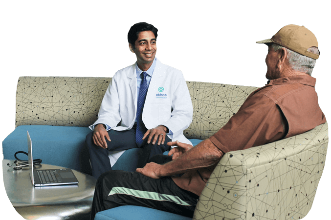 Dr. Aleem Kanji of Ethos Endocrinology smiles as he speaks with a happy patient in a medical office in Houston, Texas.