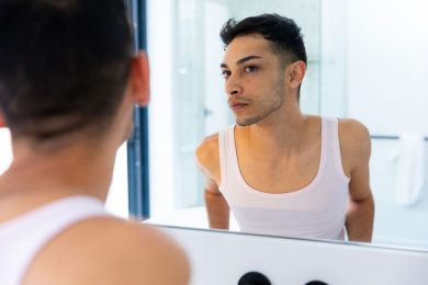 A young transgender person examines themselves in a mirror.